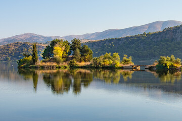 Koutavos Lagoon's serene waters mirror the charming town of Argostoli under a vast blue sky. Lush greenery frames the tranquil scene, offering a peaceful escape in the heart of Kefalonia, Greece.