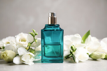Bottle of perfume and beautiful flowers on light table
