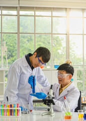 Close up of asian professional senior doctor scientist teach and guide asian young scientist looking test tube with blue liquid substance in working laboratory.