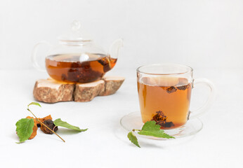 Chaga tea in a glass mug and teapot on a white background. Trendy healthy beverage. Drink with pieces of birch mushroom.