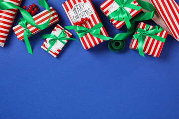 Christmas gift boxes with green bows on blue background, flat lay. Space for text