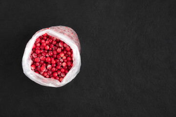 Frozen cranberry berries in a bag on a black background. Stocks concept. Frozen food. Copy space, top view, flat lay.