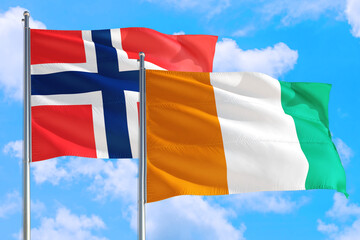 Cote D'Ivoire and Bouvet Islands national flag waving in the windy deep blue sky. Diplomacy and international relations concept.