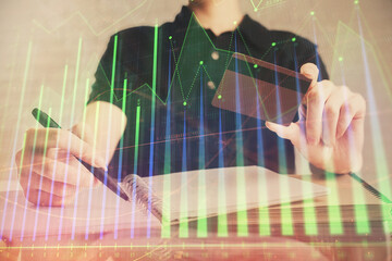 Double exposure of man hands holding a credit card and Forex graph drawing. Stock trading and digital fintech in Internet E-commerce concept.
