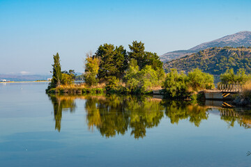 Fototapeta premium Koutavos Lagoon's serene waters mirror the charming town of Argostoli under a vast blue sky. Lush greenery frames the tranquil scene, offering a peaceful escape in the heart of Kefalonia, Greece