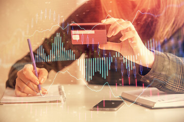 Double exposure of woman on-line shopping holding a credit card and financial graph drawing. Stock market E-commerce concept.