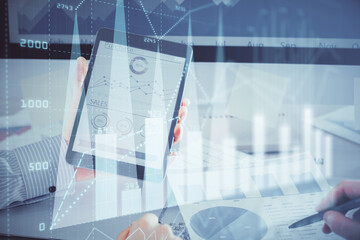 Double exposure of man's hands holding and using a digital device and forex graph drawing. Financial market concept.