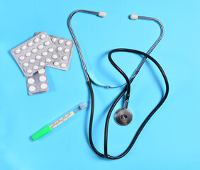 a stethoscope and medicine with a thermometer on a blue background. concept of treatment of...