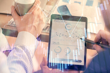 Double exposure of man's hands holding and using a phone and financial chart drawing. Market...