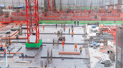 The  employee wearing safety uniform working in the construction site with red cranes and steel pillar for build modern residential area