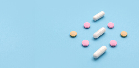 Scattered Pills on a blue background , Medicine concept. Multiple long and round white capsules and hard pills on a blue. Colorful pattern of pills and capsules on a blue.