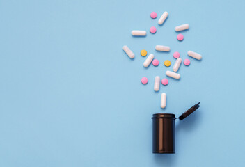 Opioid epidemic, painkillers and drug abuse concept with close up on a bottle of prescription drugs and hydrocodone pills falling out of it on blue background. Drugs, medication indoors on table, shot
