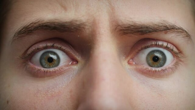 Close up of Man's face . Boy opening blue eyes wide looking around. Concept of fear, terror, horror. Male model with pretty blue, green, grey eyes. Slow-motion, macro extreme close-up, 4K.