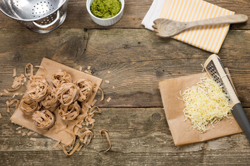 Wholemeal tagliatelle pasta prepared for cooking. Cheese, wild garlic and wallnut homemade pesto. Served on wooden table in vintage style