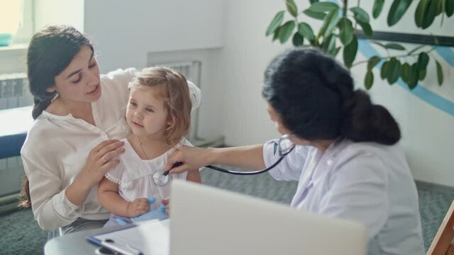 Female Doctor Pediatrician Using Stethoscope Listen to the Heart of Happy Healthy Cute Kid Girl at Medical Visit With Mother in the Hospital. Female Doctor Examining Child.