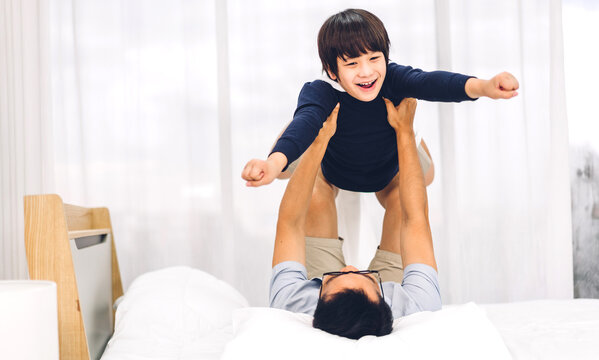Portrait of enjoy happy love asian family father carrying little asian boy son smiling playing superhero and having fun moments good time on bed at home