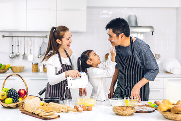 Obraz na płótnie Canvas Portrait of enjoy happy love asian family father and mother with little asian girl daughter child having fun cooking together with baking cookies and cake ingredients on table in kitchen