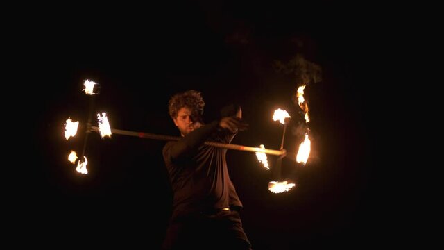 Fire show artist man spin a fire pole around his body under a bridge. Slow motion