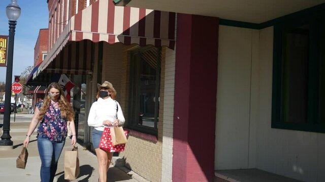 Two women wearing masks during covid pandemic shop in small American town in daytime.