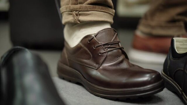 Close-up of male foot with unrecognizable man trying to put on brown boot. Male client trying on too small shoe in store. Shopping and buying.