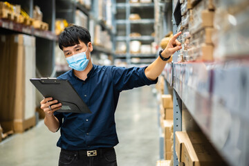 man worker with medical mask holding clipboard and checking inventory in warehouse during coronavirus (covid-19) pandemic
