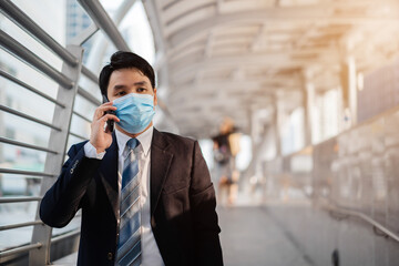 business man talking on mobile phone and wearing medical mask during coronavirus (covid-19) pandemic in city
