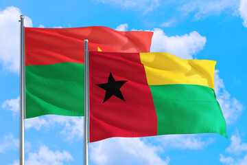Guinea and Burkina Faso national flag waving in the windy deep blue sky. Diplomacy and international relations concept.
