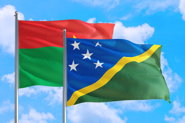 Solomon Islands and Burkina Faso national flag waving in the windy deep blue sky. Diplomacy and international relations concept.
