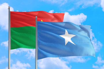 Somalia and Burkina Faso national flag waving in the windy deep blue sky. Diplomacy and international relations concept.