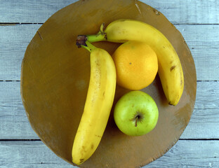 
two bananas and an apple with an orange lie on a wooden plate