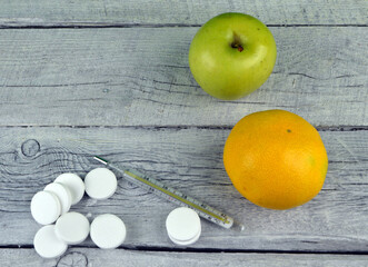 
thermometer and pills as well as fruits lie on a wooden background
