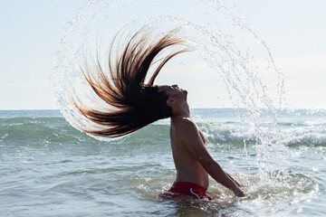 Closeup shot of a young man with long hair doing a hair flip in the water