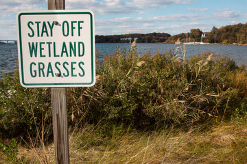 Stay Off Wetland Grasses sign at the grassy edge of blue water.