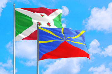 Reunion and Burundi national flag waving in the windy deep blue sky. Diplomacy and international relations concept.