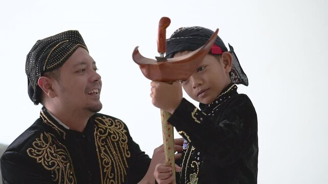 A portrait of a father tidy up his son's javanese clothes. beskap and blangkon