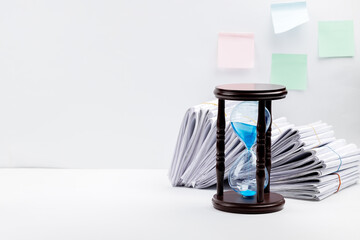 paperwork deadline concept. side view for a minimal workspace with big heap of files and hourglass...