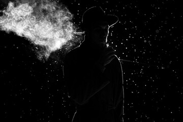 dark silhouette of a man in a hat Smoking a cigarette in the rain