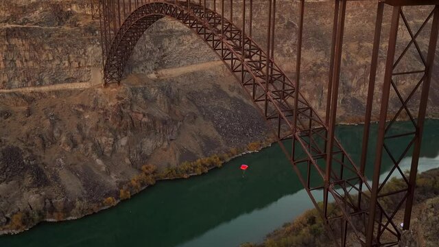 This epic video shows a person with a red parachute base jumping off a mountainous bridge at sunset with a river below.