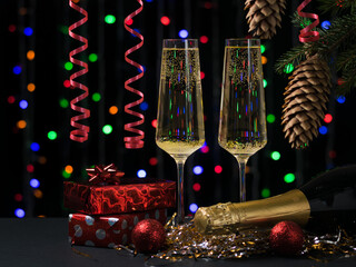 Two glasses with a bottle of champagne, gifts and a Christmas tree on the background of bokeh.