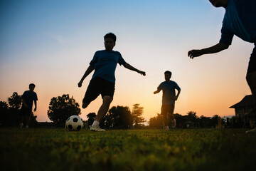 Silhouette action sport outdoors of a group of kids having fun playing soccer football for exercise in community rural area under the twilight sunset. 