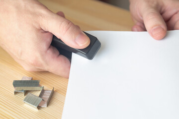 The hand with a stapler connects documents. Copy space.