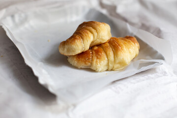 Two small fresh traditional Argentine croissants lie on white wrapping paper on the kitchen table in the house