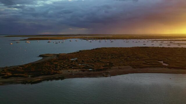 An aerial flight over the salt marshes at West Mersea, Essex just before a storm with dramatic light over the water.