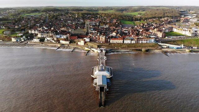 Drone footage from the sea flying over the pier at Cromer, Norfolk towards the town in early morning.