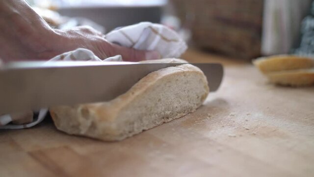 Close up of a slice of white bread being cut from a loaf on a wooden cutting board. Slow motion with shallow depth of field. 