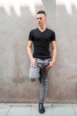 Full length shot of handsome young Italian man with undercut leaning against wall outdoors while thinking