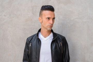 Handsome young Italian man with undercut wearing black leather jacket while thinking