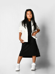 Profile of self-confident asian girl in black long t-shirt dress and white blazer and sneakers looking at camera