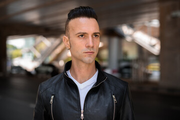 Face of handsome young Italian man with undercut wearing black leather jacket outdoors while thinking