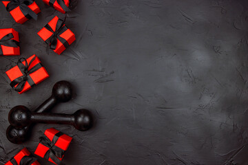 A pair of dumbbells and red gifts with black ribbons on a black background.  Holiday fitness sale or black friday concept.